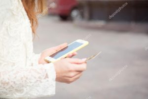 Close up female hands with a phone and a credit card on the background of the road and a car.